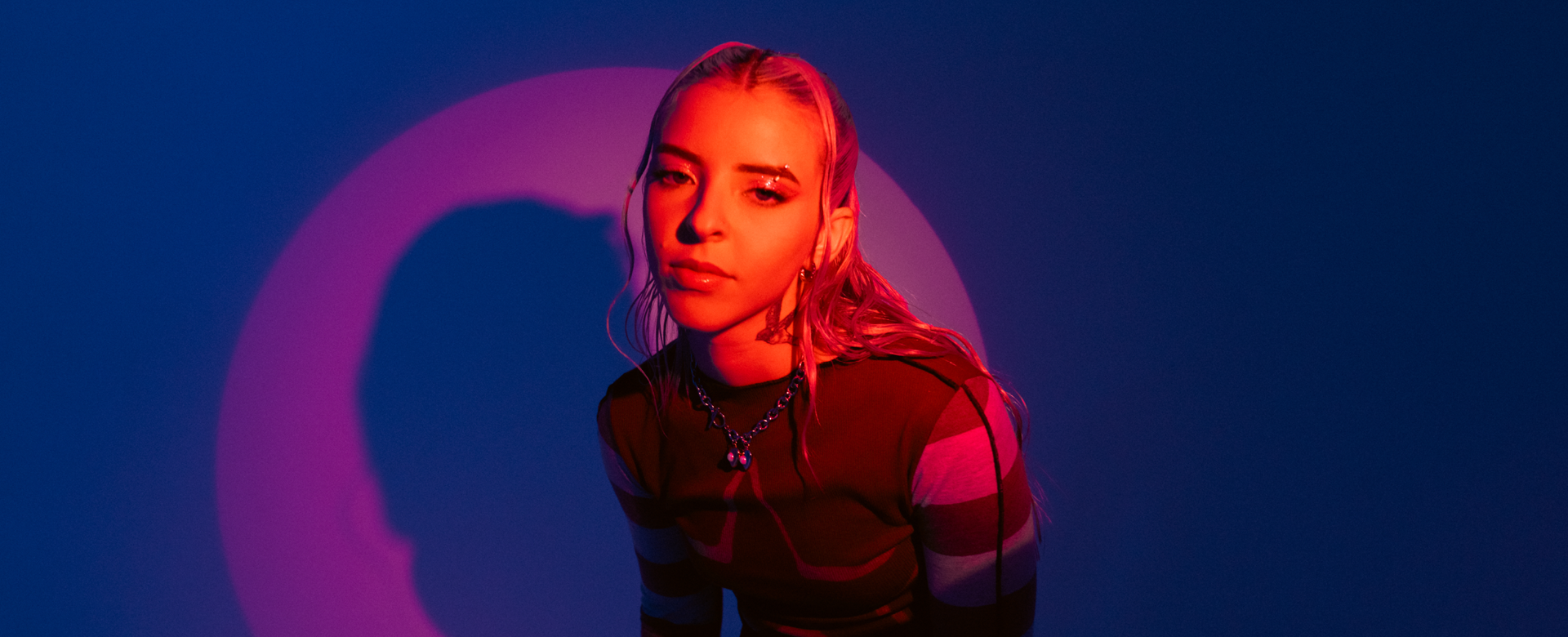 Young Miko in pink light against a blue and pink background